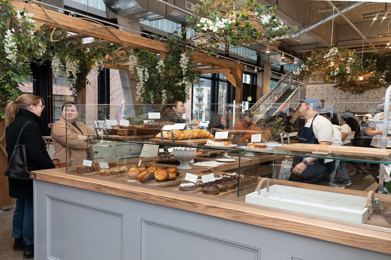 A man standing behind a counter filled with pastries talking to customers in line.