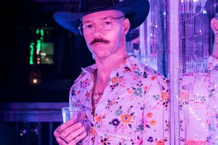 Dave Wrangler wearing a cowboy hat and holding a glass in his hand.