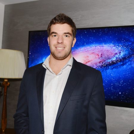 Wide shot of Billy McFarland standing in front of a television screen.