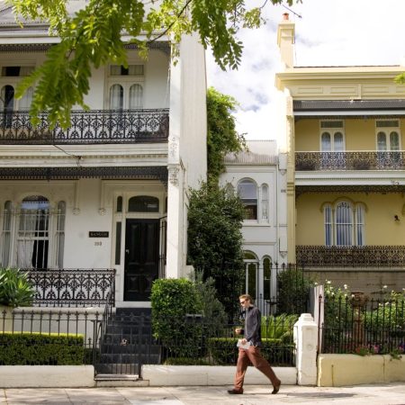 A row of townhouses on a sunny day with a pedestrian walking in front of them.