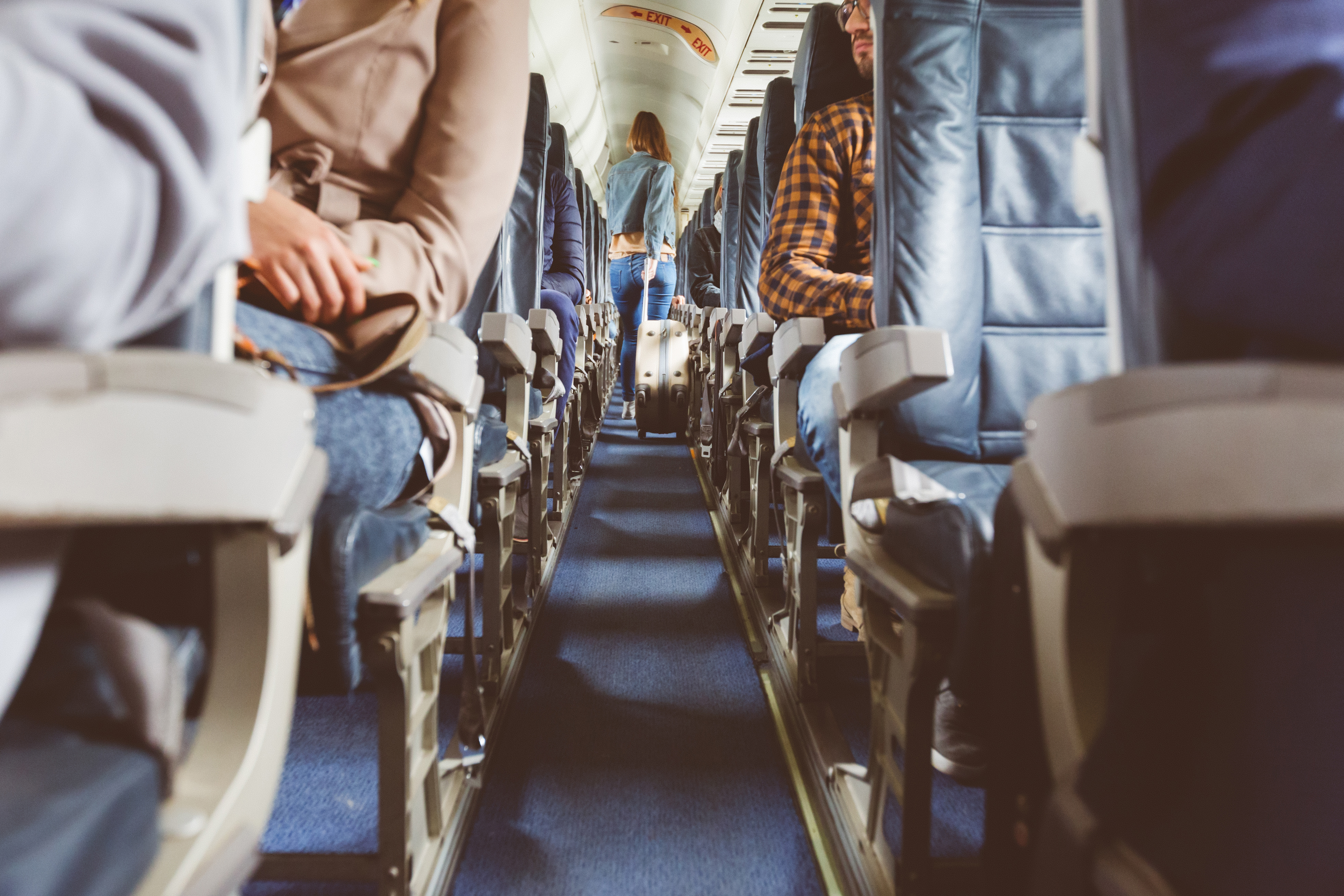 Interior of airplane with people sitting in seats. Passengers with suitcase in aisle looking for seat during flight.