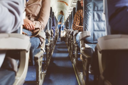 Interior of airplane with people sitting in seats. Passengers with suitcase in aisle looking for seat during flight.