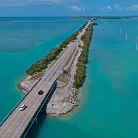 Highway going across small strip of land on top of large blue body of water.