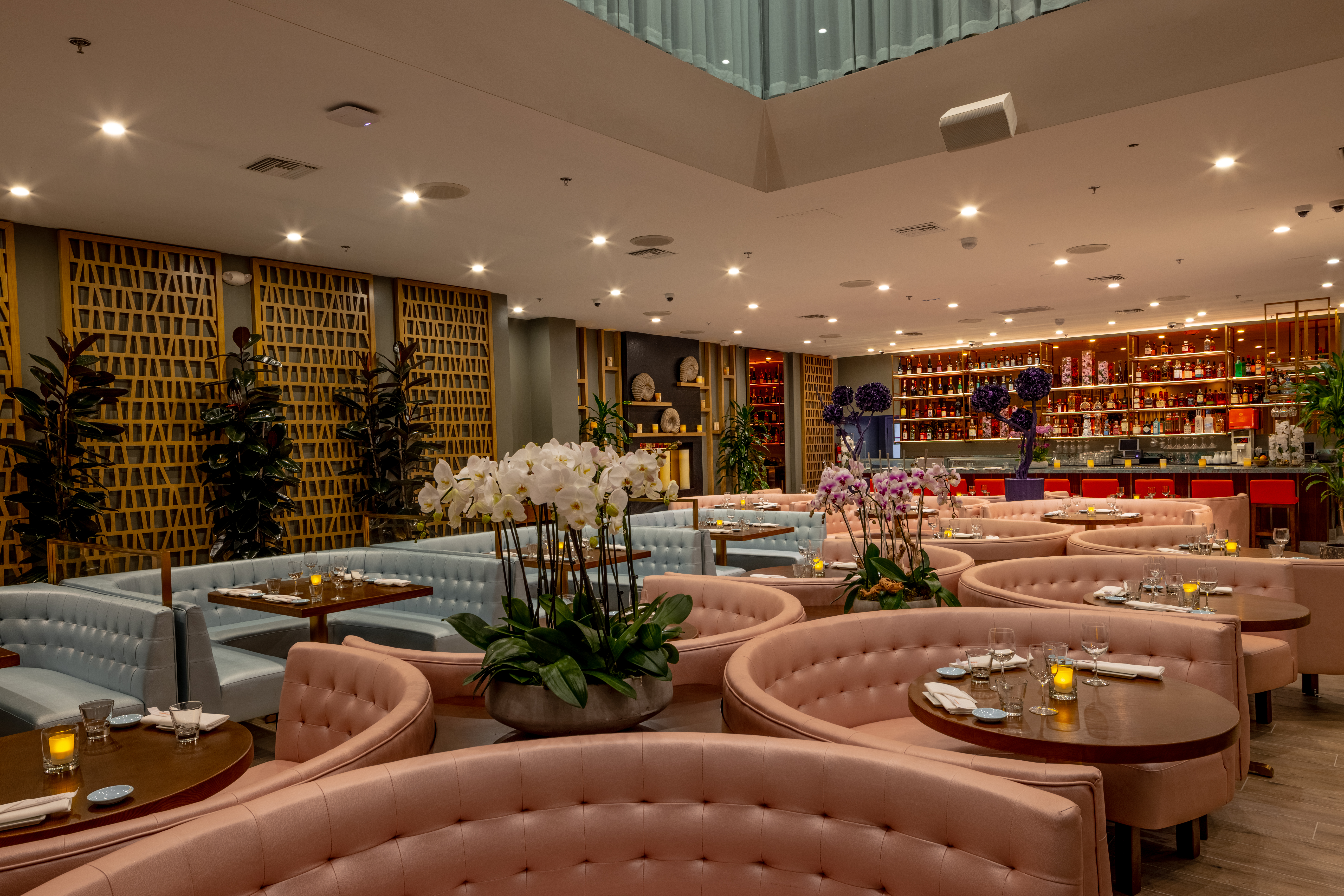 Pink and blue booth seats at round tables in front of a colorful bar