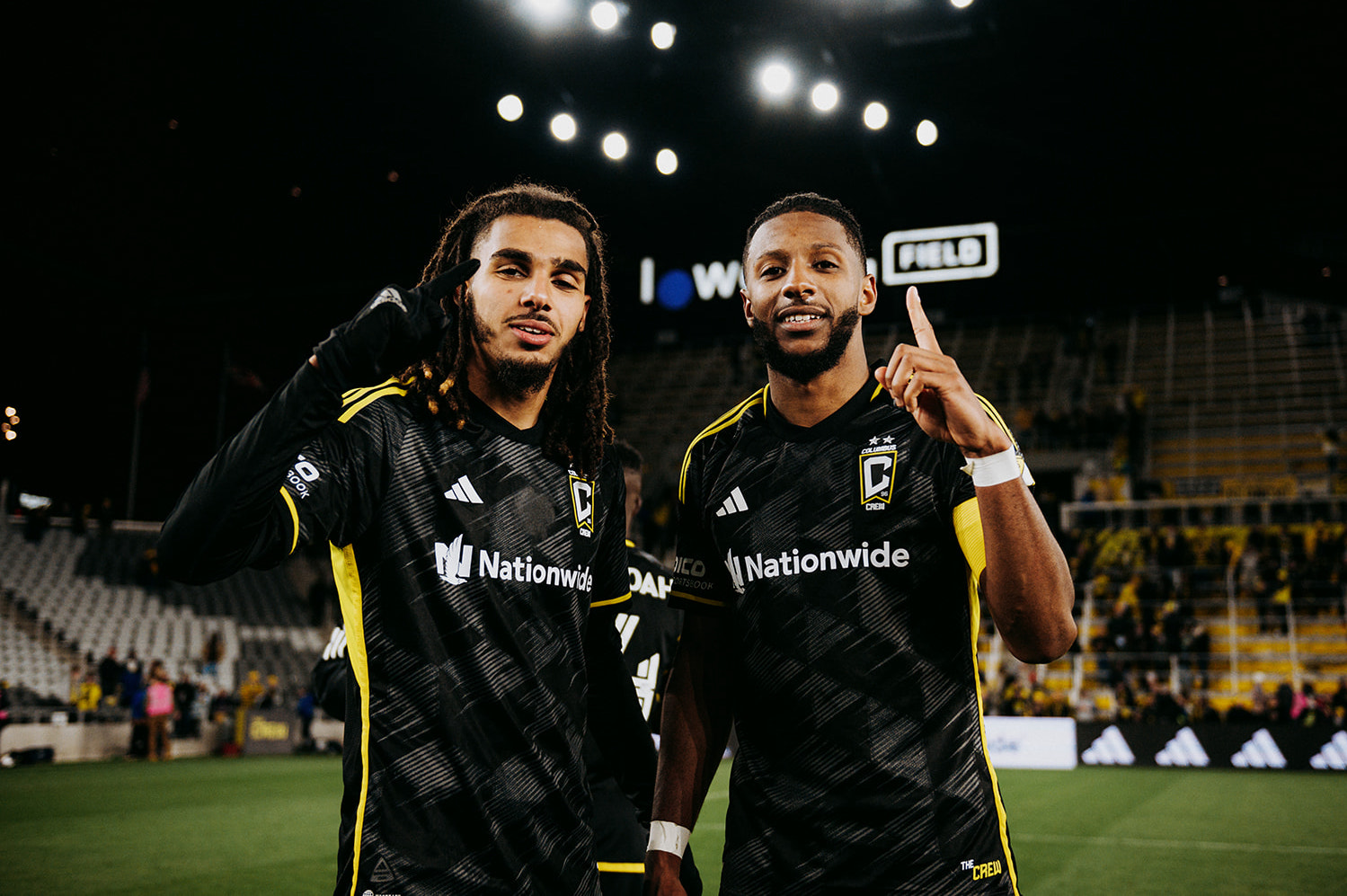 Mohamed Farsi and Steven Moreira of the Columbus Crew soccer club in MLS pose for a picture, their index fingers pointing up, on the pitch at their home stadium, Lower.com Field