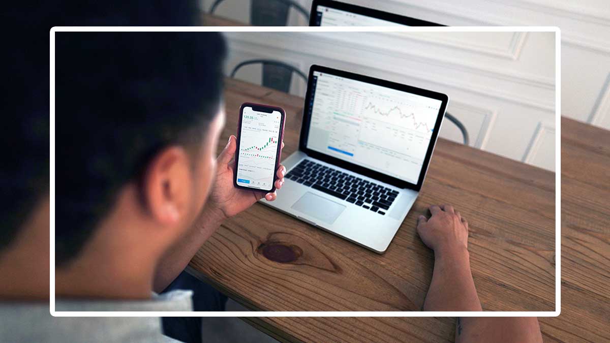 A man looking at stocks on his phone and laptop