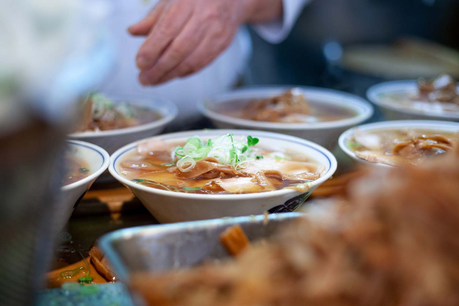 Six bowls of ramen, with one centrally placed, topped with scallions and menma
