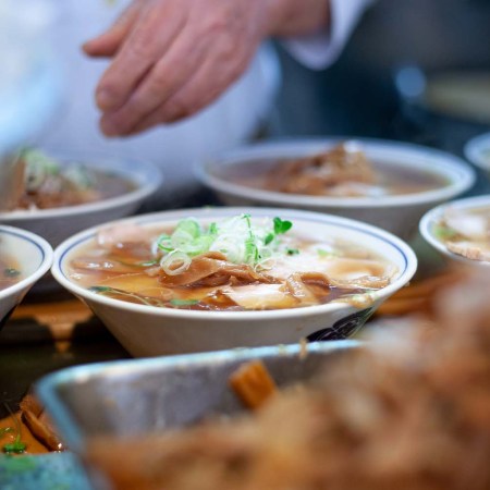 Six bowls of ramen, with one centrally placed, topped with scallions and menma