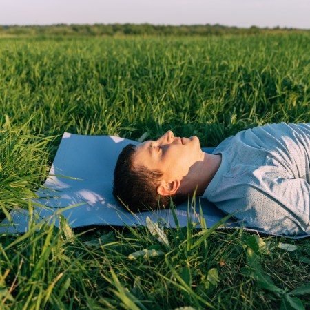 A man laying in a field breathing through his nose.