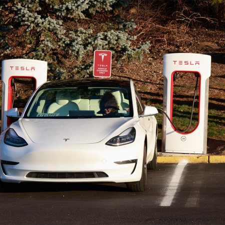 A person sitting in a Tesla EV at a charging station. According to reporting from Reuters, Tesla employees inappropriately shared images and videos recording by Tesla cars in an internal messaging system.