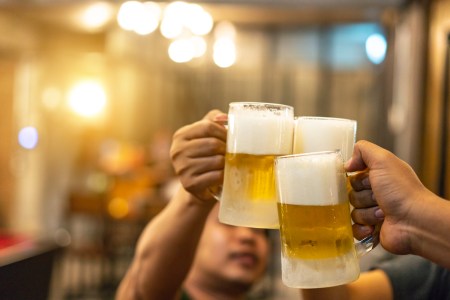 Beer glasses raised in a toast. Close-up hands with glasses. Blurred bar interior at the background