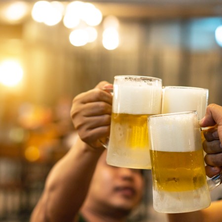 Beer glasses raised in a toast. Close-up hands with glasses. Blurred bar interior at the background