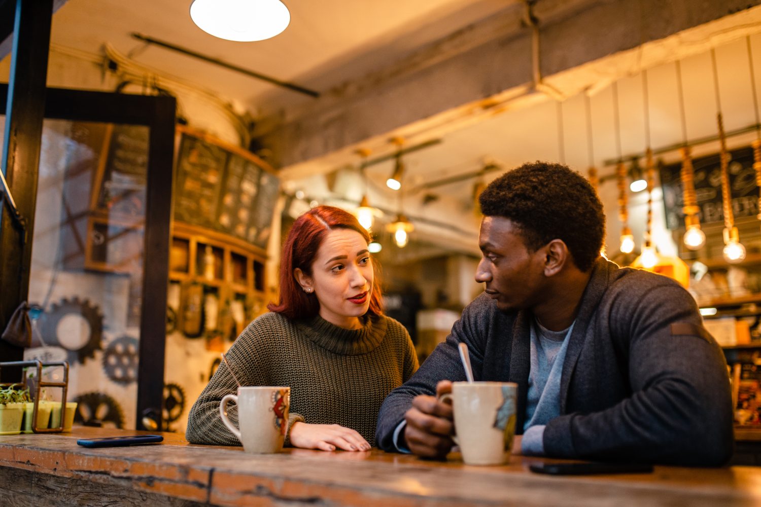 two people sitting and talking next to each other with coffee mugs.
