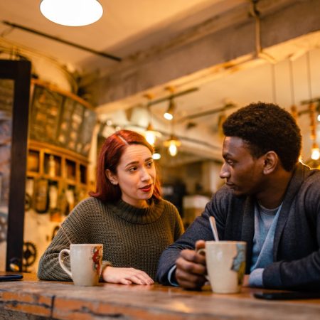 two people sitting and talking next to each other with coffee mugs.