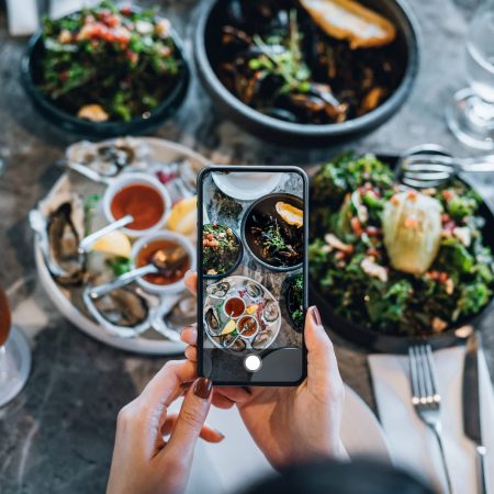 Overhead view of an influencer taking a photo of their food. Today, we look at the 10 food and drink Instagram accounts in Texas worth following.