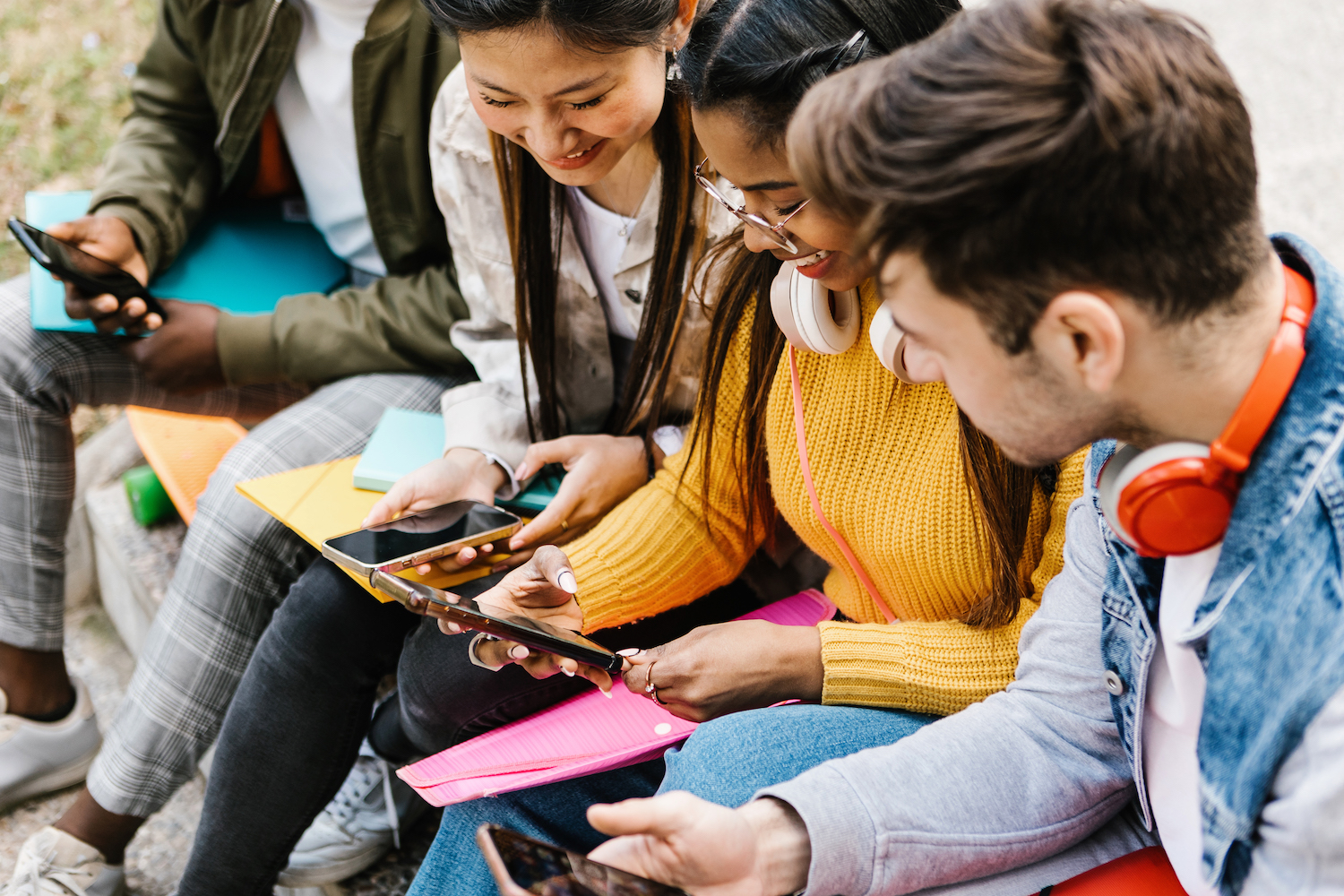 Diverse young teenage students having fun using mobile phone in college campus