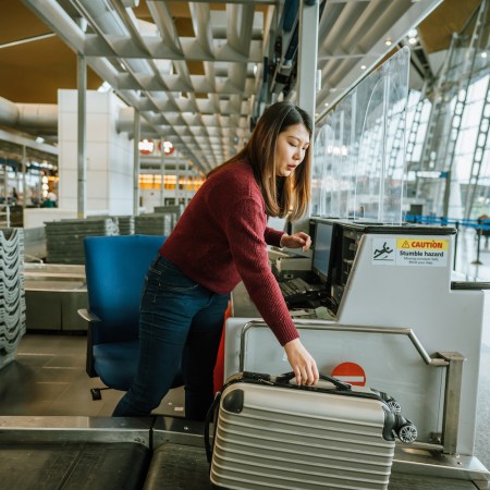 Young female airline check-in assistant putting luggage on the scales at check-in counter in airport