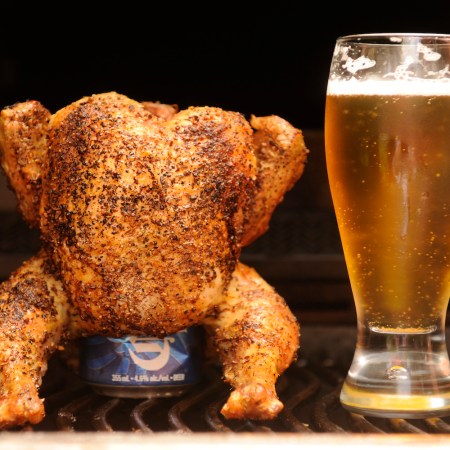 a full cooked chicken with a beer can inside of it and standing upright next to a glass of beer
