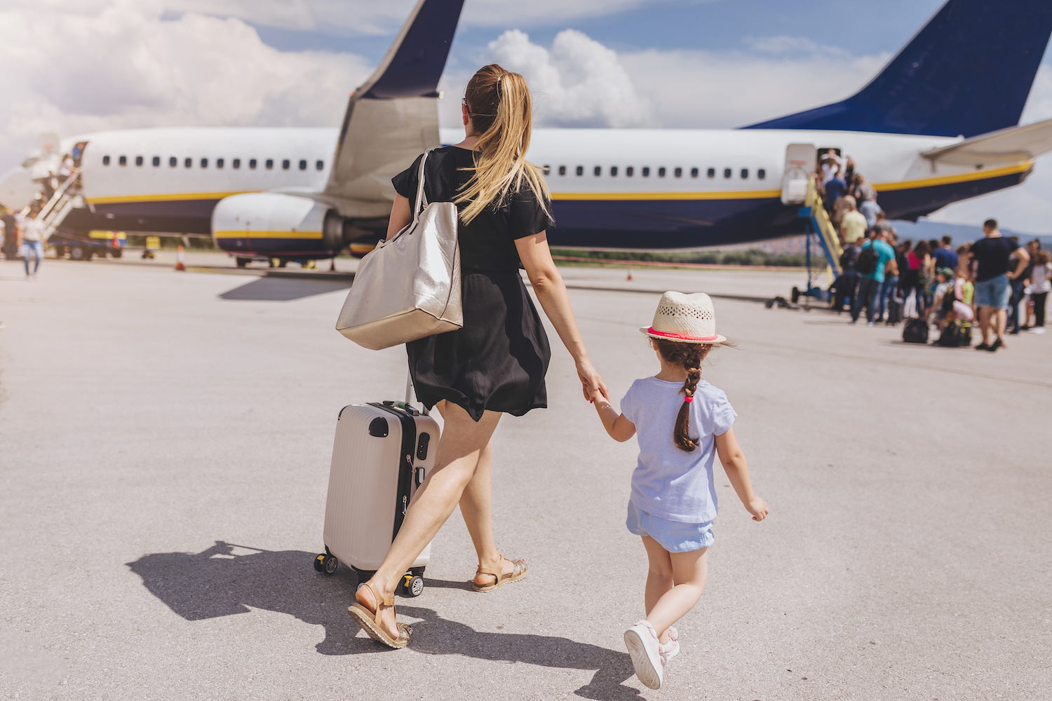 Mother and daughter holding hands while boarding a plane outside