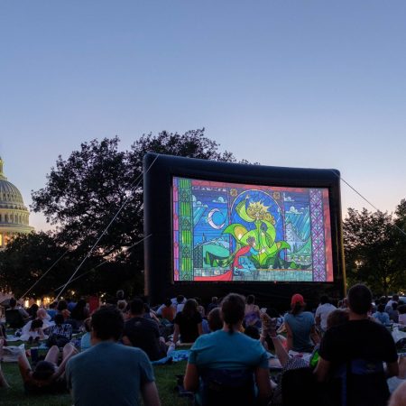 Capitol Hill behind projector screen showing movie on a lawn with people watching in Washington, D.C.