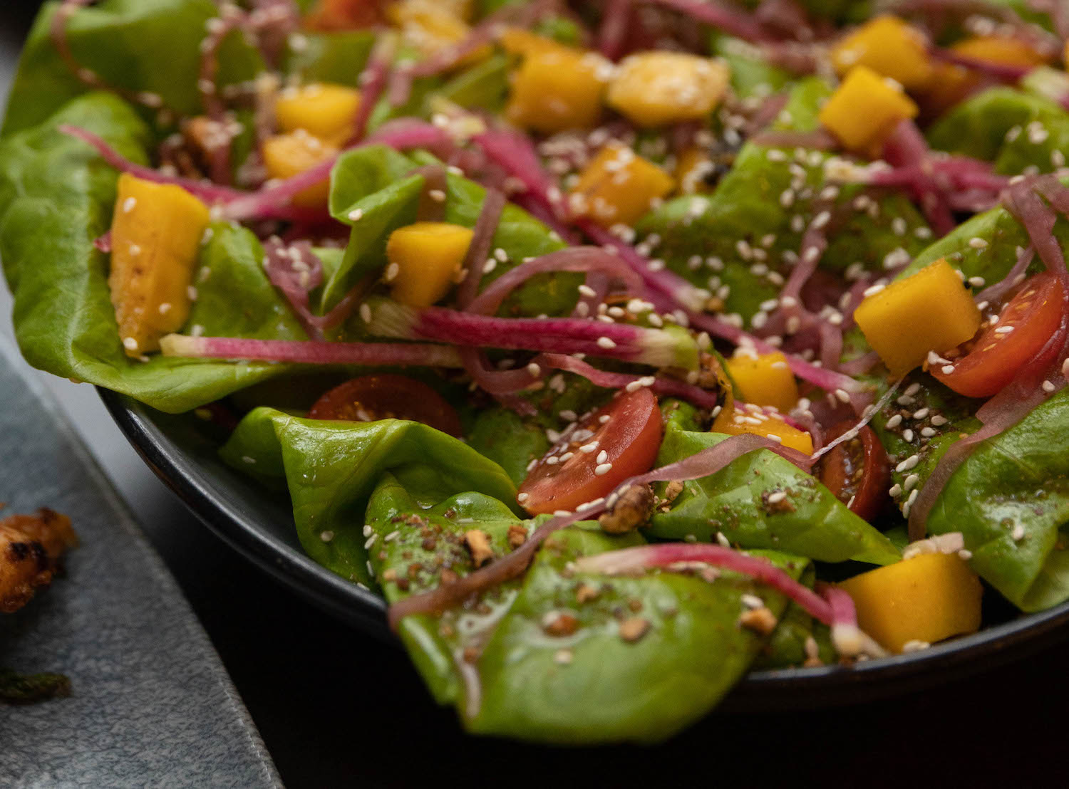 tomatoes, onions, mangoes, dressing and seeds on top of bed of spinach in a bowl
