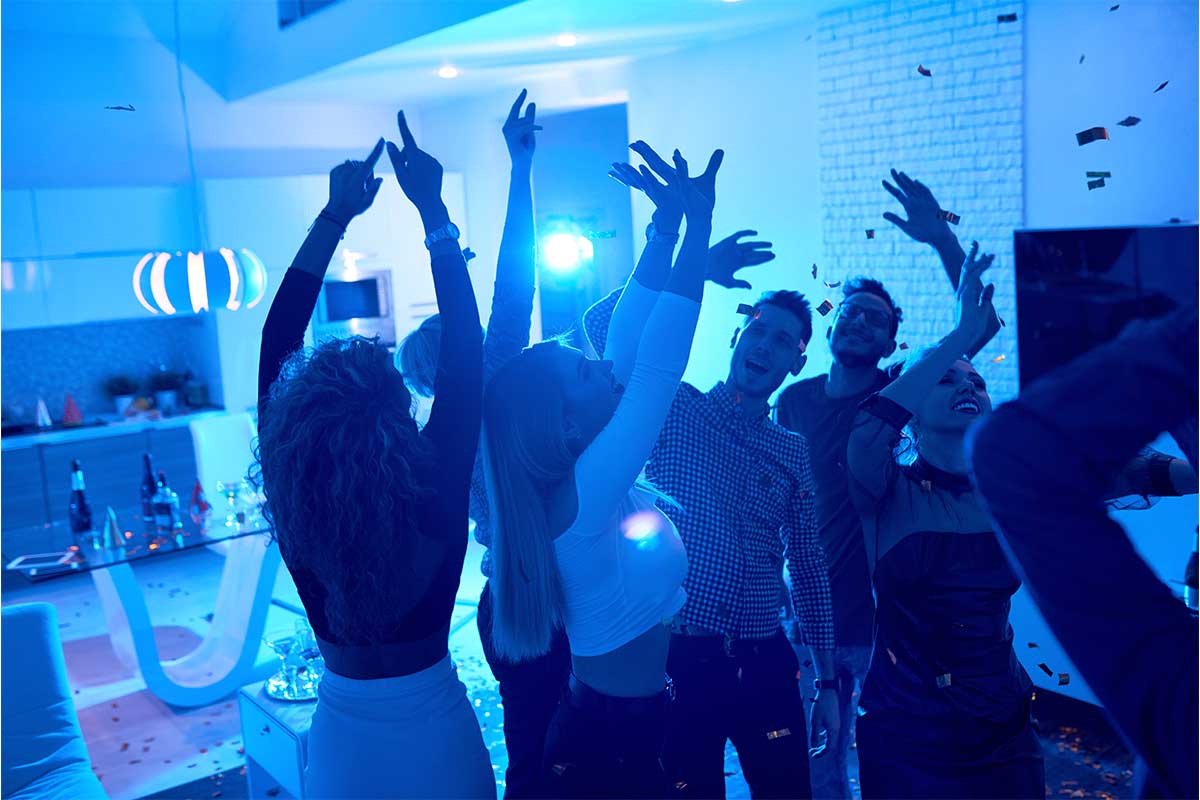 Group of modern young people dancing under confetti at private house party lit by blue light. Airbnb has announced an anti-party crackdown for Memorial Day.