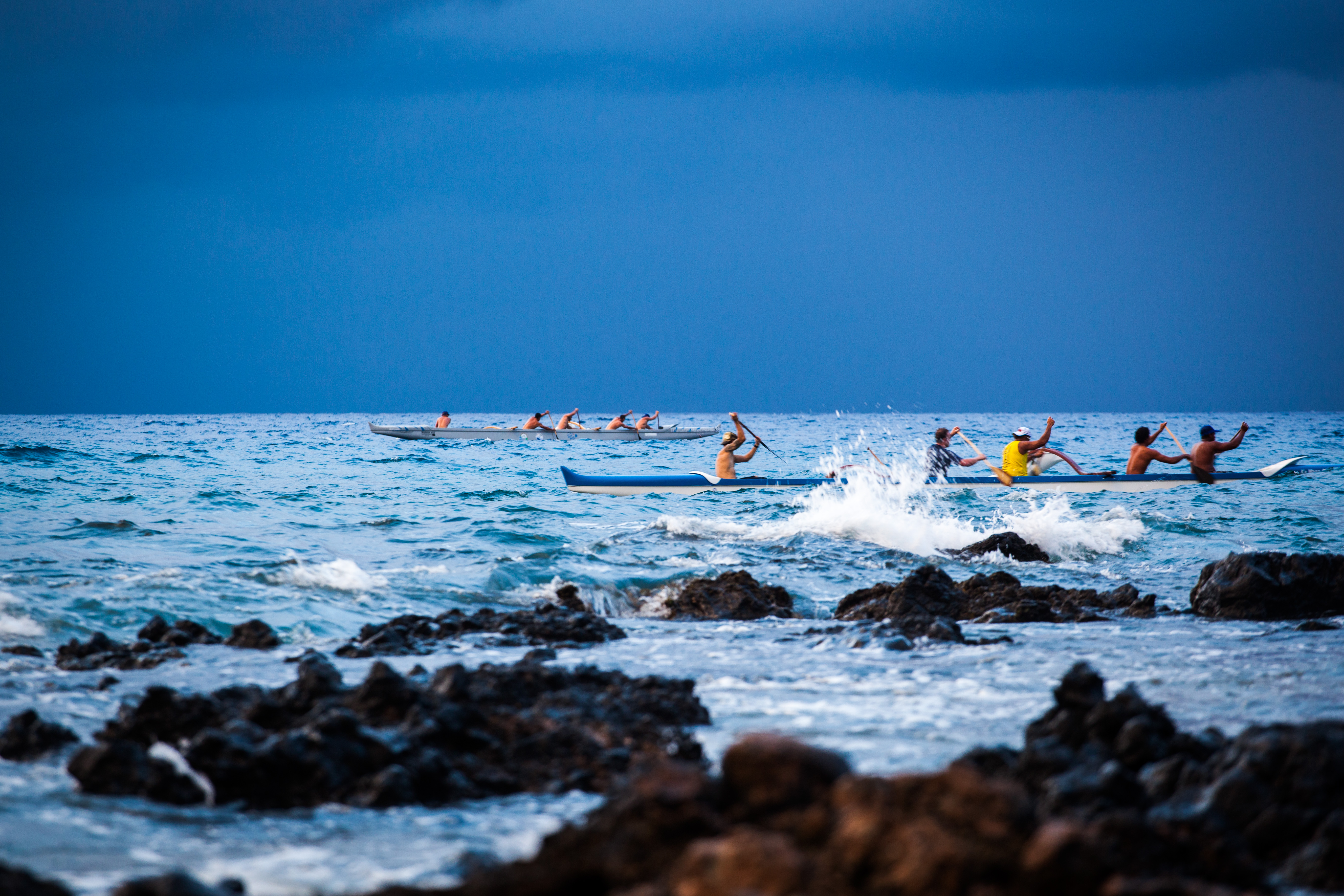 Men paddling canoes in blue water.