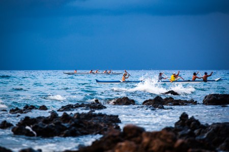 Men paddling canoes in blue water.