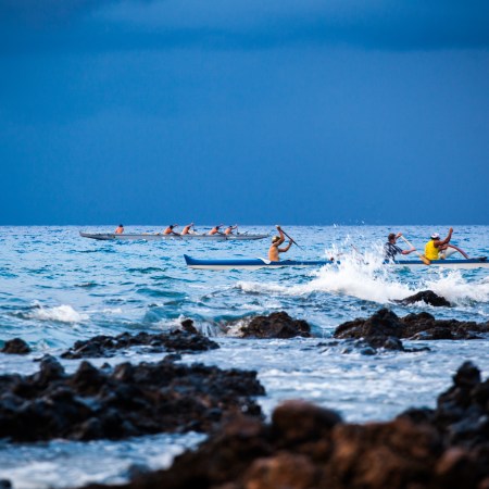 Men paddling canoes in blue water.