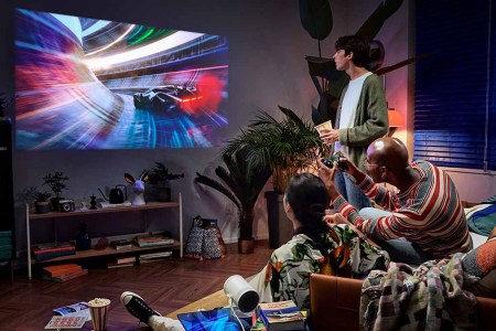 The Freestyle by Samsung in a living room where three people are playing video games. The Discover Samsung Event features discounts across the tech brand's portfolio.
