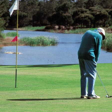 An old man putting on a golf green.
