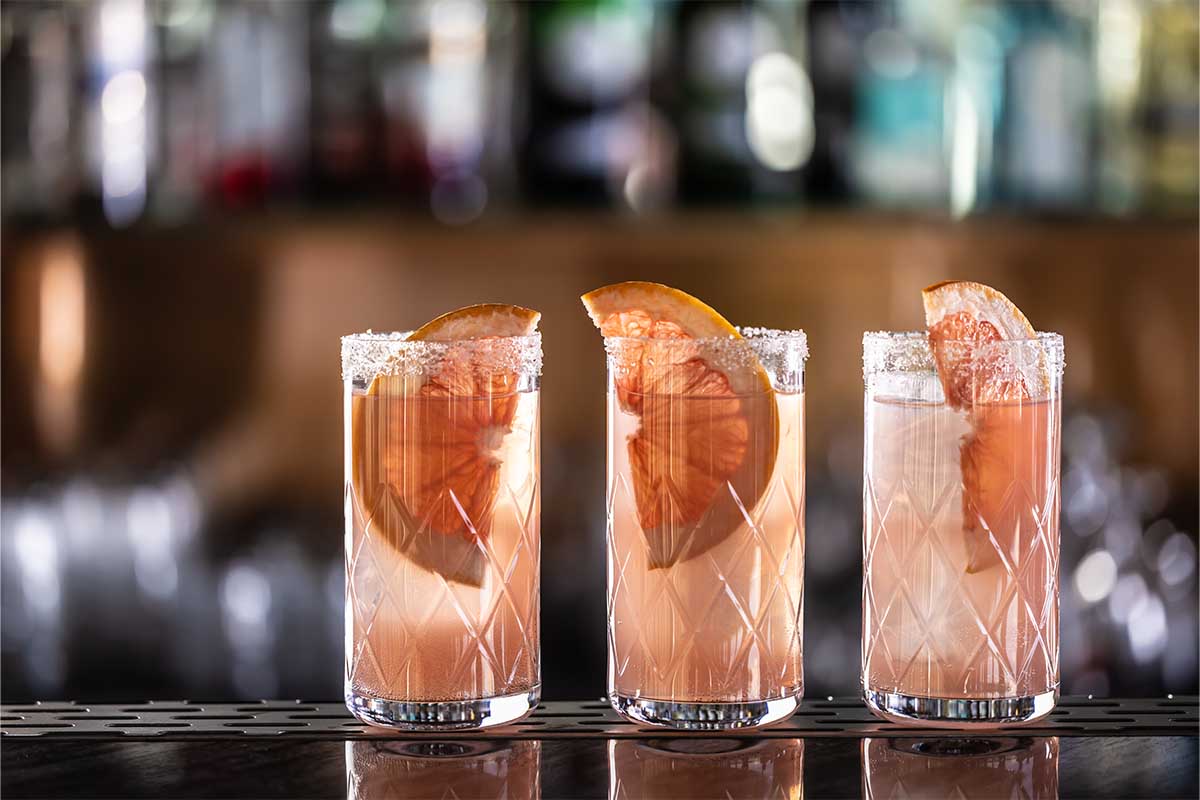 Three paloma cocktails garnished with grapefruit placed on the bar counter.