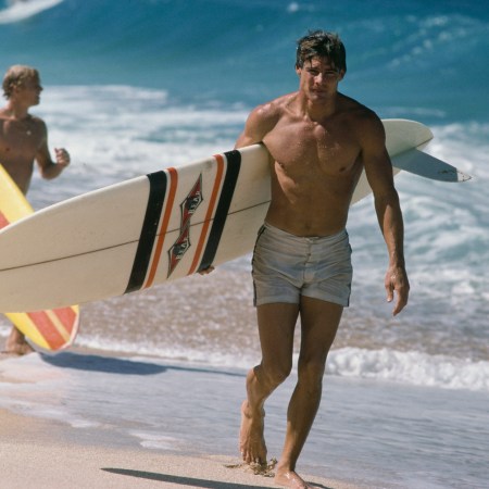 An actor playing a surfer, walking down the beach.