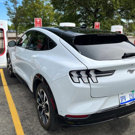 A white Ford Mustang Mach-E at a Tesla Supercharger charging station.