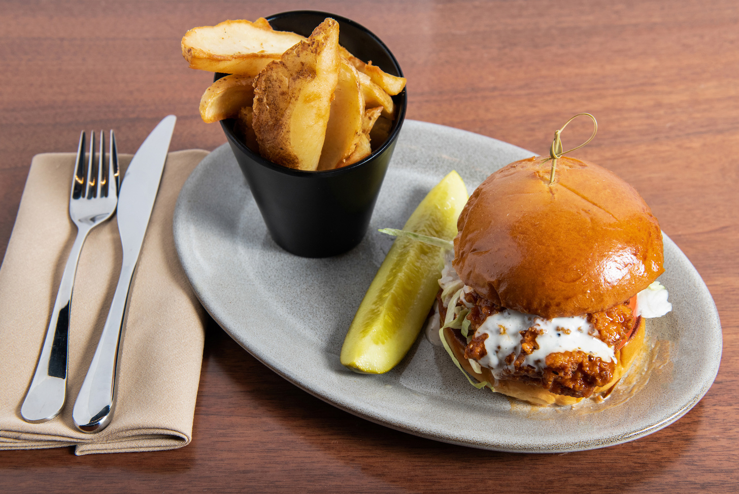 buffalo chicken sandwich on a plate with a pickle and cup of fries.