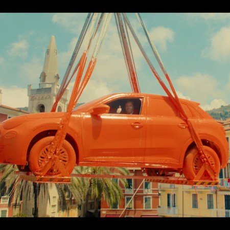 A Fiat completely dipped in orange paint emerges from a gray tank by crane