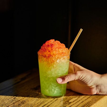 green slush-like cocktail with red on top and someone holding the cup