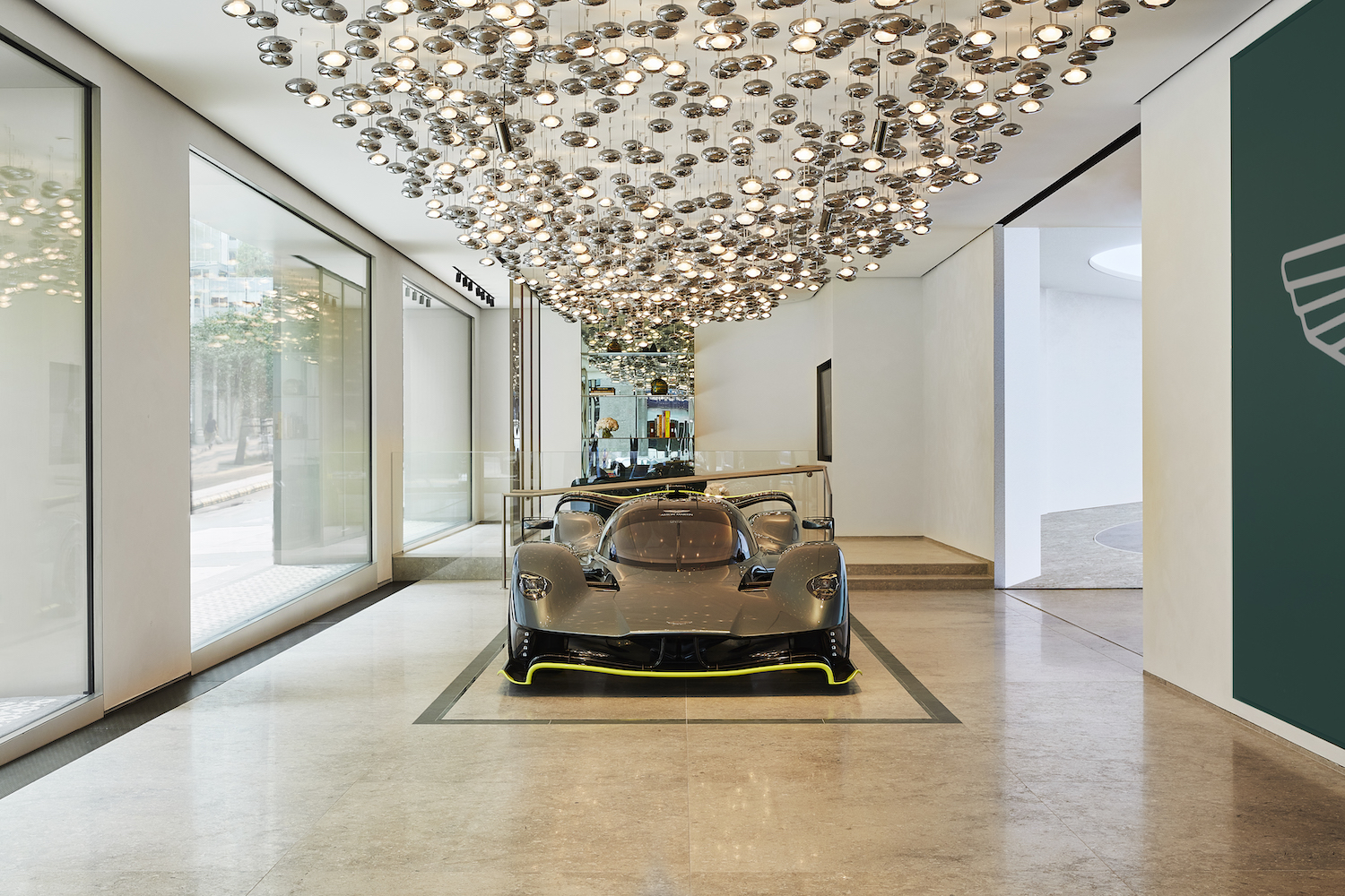 Car under chandelier next to big windows.