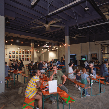 people sitting at tables in a seating area with neat lights and arcade games