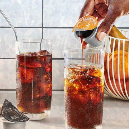 A person pouring a Cometeer coffee capsule in a glass with ice.