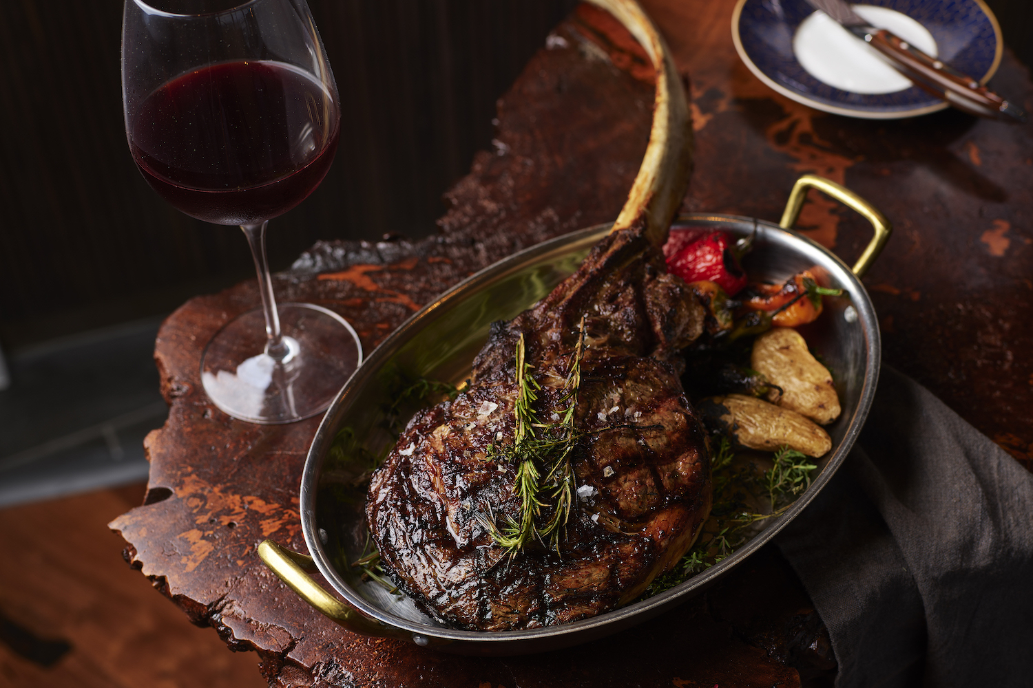 Tomahawk steak in a pan next to a glass of red wine.
