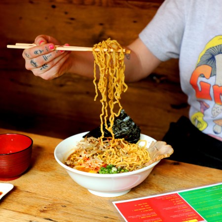 Person using chopsticks to eat ramen from a bowl.