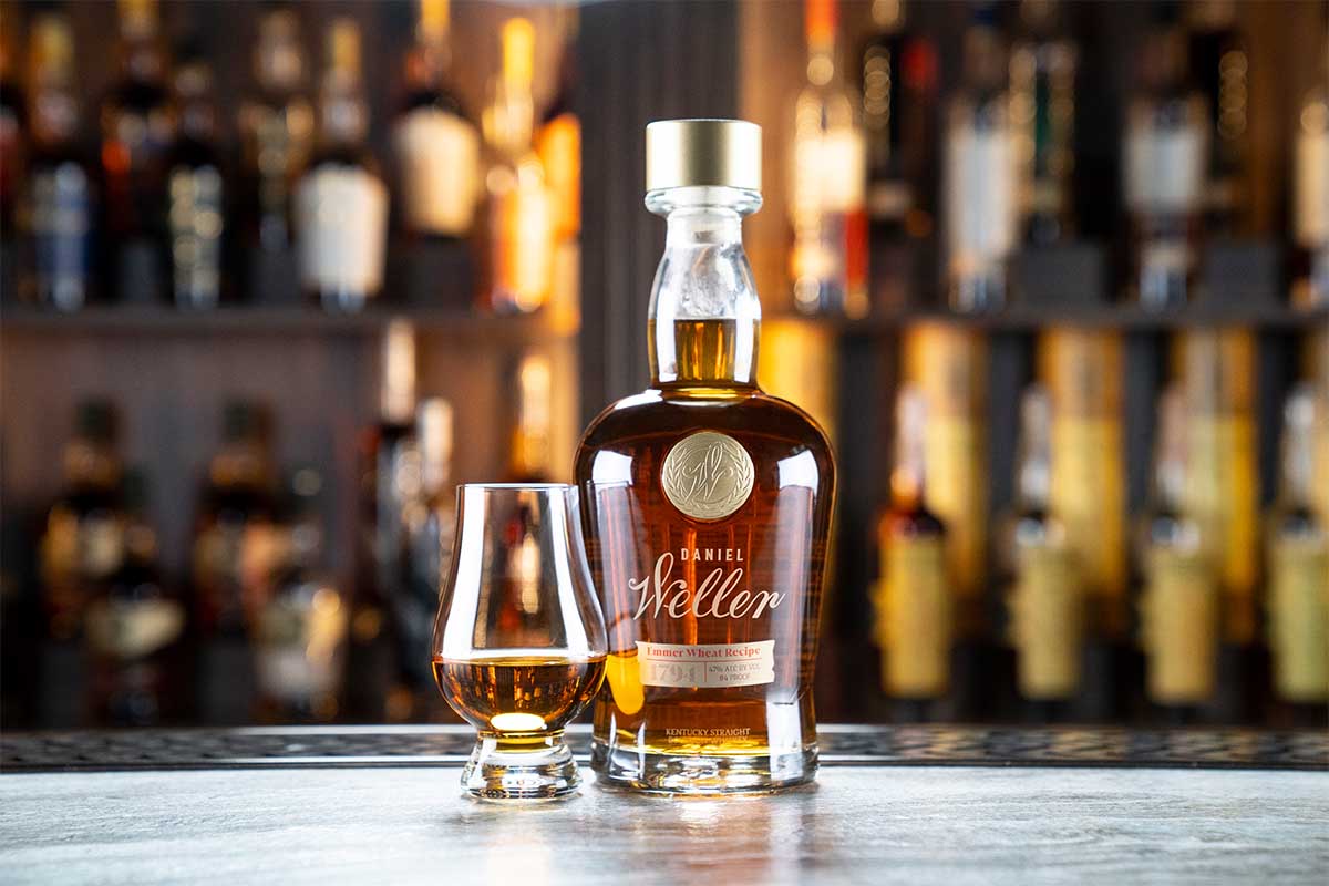 Daniel Weller Emmer Wheat bottled and a glass of whiskey on a bar counter in front of other Buffalo Trace releases. The new whiskey utilizes a long-forgotten grain called Emmer.