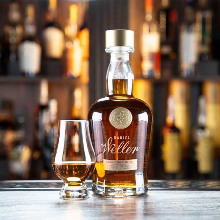 Daniel Weller Emmer Wheat bottled and a glass of whiskey on a bar counter in front of other Buffalo Trace releases. The new whiskey utilizes a long-forgotten grain called Emmer.
