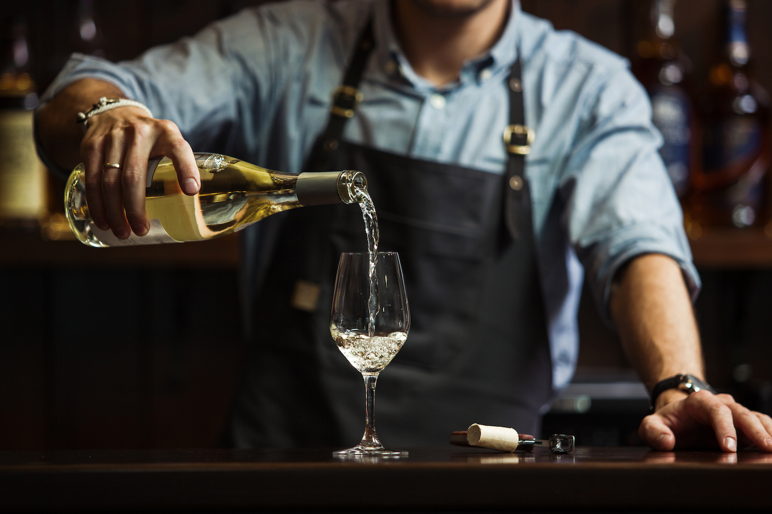 Male sommelier pouring white wine into long-stemmed wineglasses.
