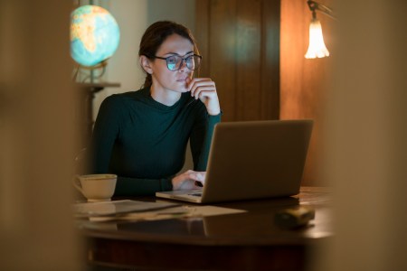 professional woman working in her home study at night with a laptop on the table