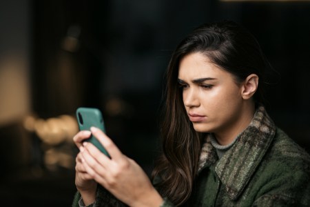 Close up of a depressed Caucasian young woman sitting at home, reading some bad news on her smart phone, feeling sad and worried