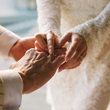 Bride putting ring on groom's finger. Rings exchange. Happy couple celebrating wedding outdoors in summer.