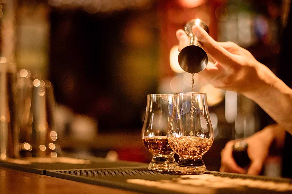 Whiskey being poured into two Glencairn glasses on a bar counter