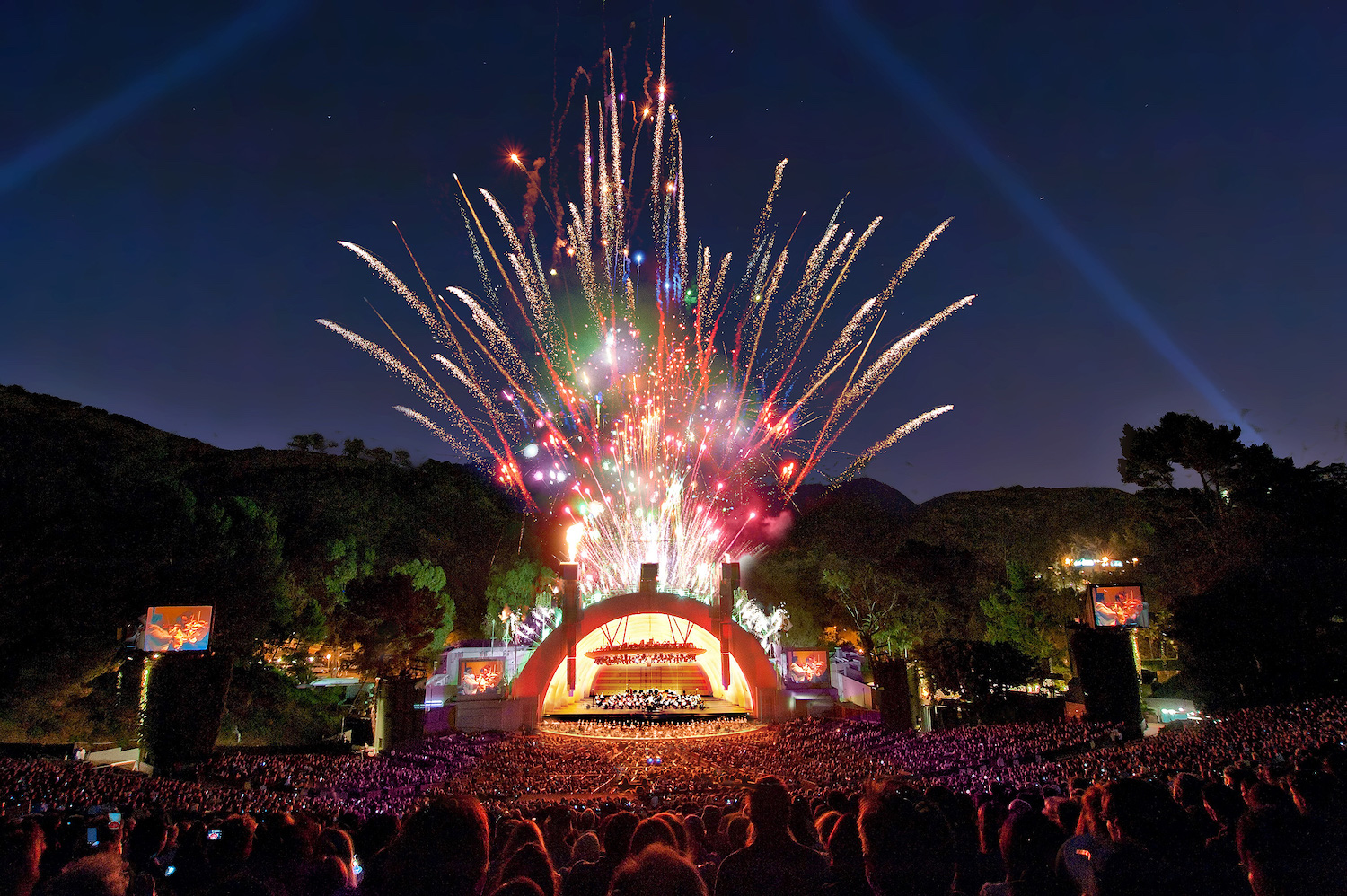 fireworks blasting in the air over a crowd and stage